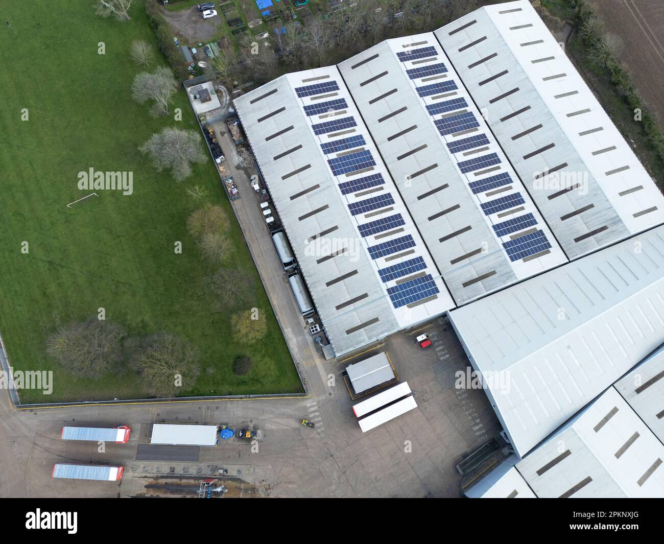 Drone vista dall'alto verso il basso di un grande magazzino che mostra pannelli solari parziali sui tetti. I camion e i rimorchi possono essere visti nel cortile. Foto Stock