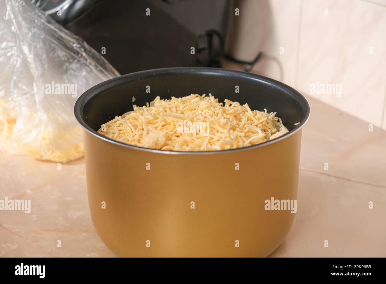 Un uomo mette il formaggio congelato dal freezer grattugiato su una grattugia in una ciotola di cucina lenta. multicooker. Cucina pranzo cena per la famiglia a casa. cuochi di processo Foto Stock