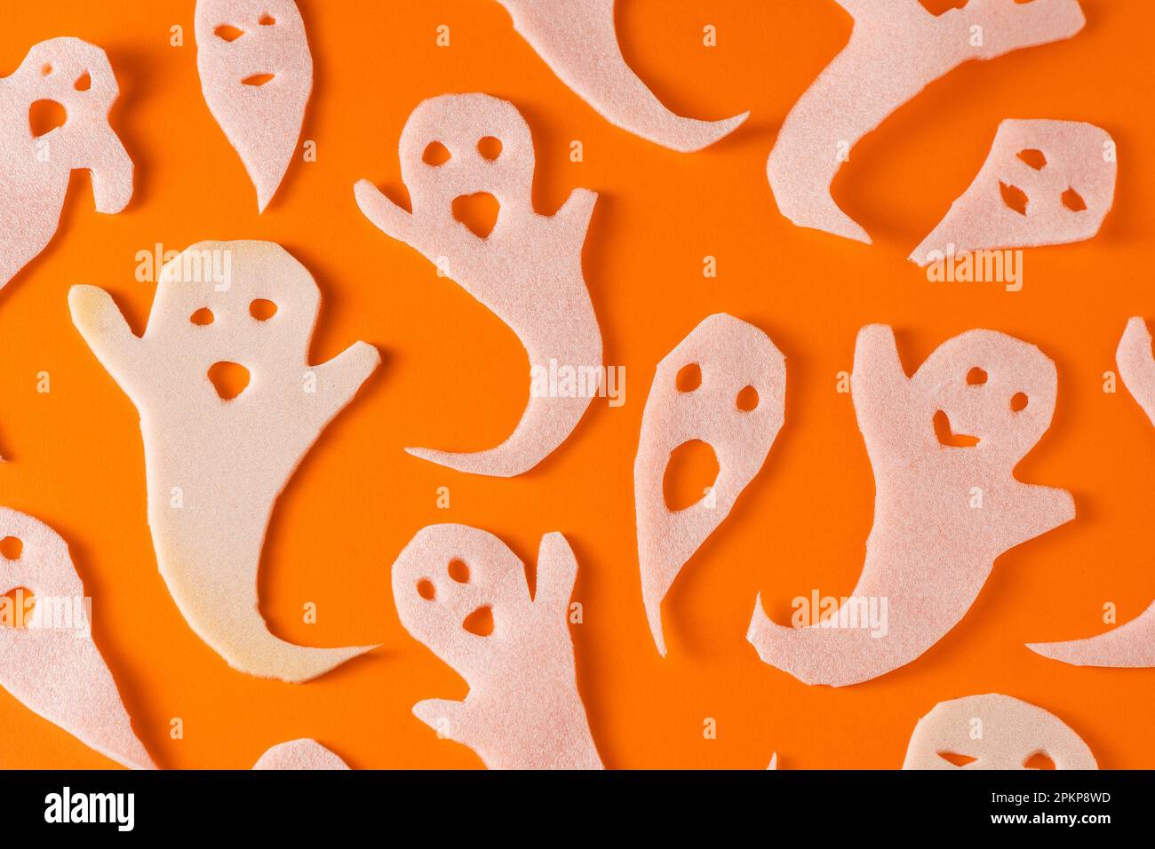 Fantasmi bianchi bambini di mestiere per Halloween. Immagine fantasma della carta di avvolgimento su sfondo arancione vista dall'alto. Un mostro pauroso e divertente giocattolo con le tue mani. Fumetto Creepy Whisper. Fai-da-te fatto a mano. Impostare i caratteri boo Foto Stock