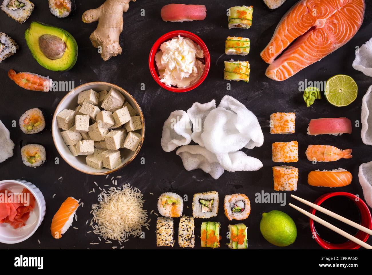 Set di piatti tradizionali giapponesi su sfondo scuro. Sushi, nigiri, bistecca di salmone crudo, riso, formaggio spalmabile, avocado, lime, zenzero sottaceto (gari) Foto Stock