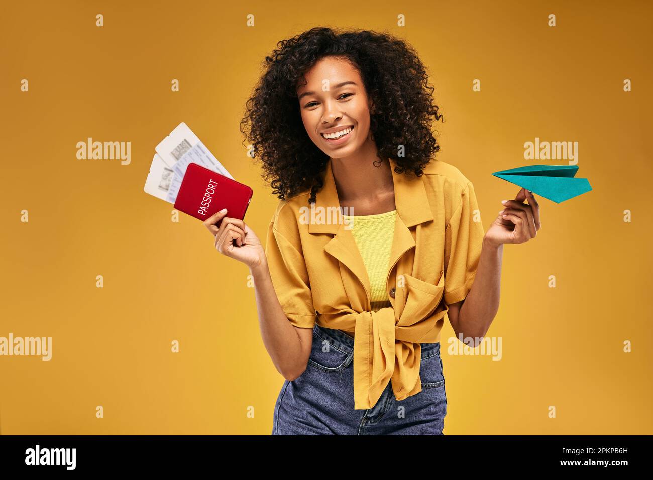 Passaporto internazionale con biglietti aerei e aereo di carta in mano a una donna afro-americana viaggiatore, su sfondo giallo. Concetto di viaggio aereo Foto Stock