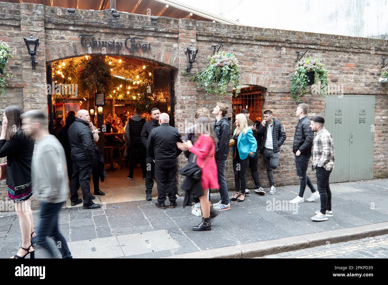 Persone in coda per entrare nella strada affollata di capra sete nel quartiere cattedrale di sabato sera Belfast City Centre, Irlanda del Nord, Regno Unito con il mot Foto Stock