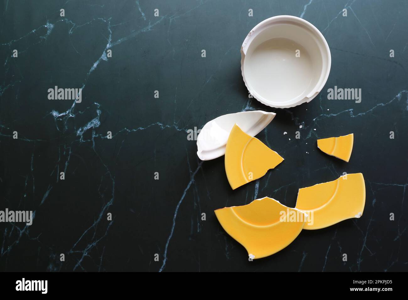 Ceramiche bianche e gialle rotte sparse sul pavimento nero Foto Stock