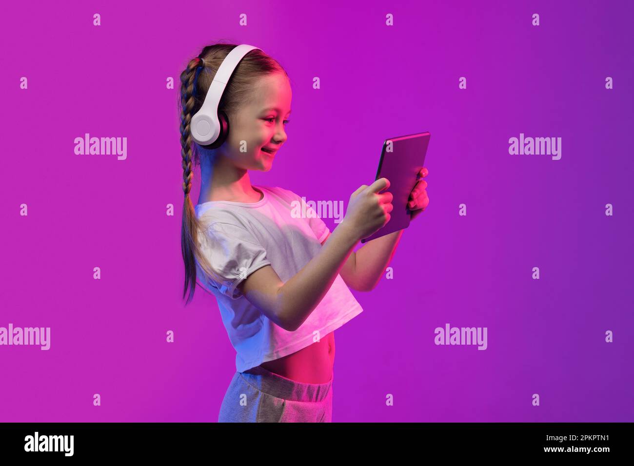 Ragazza bionda felice in età scolastica con tablet e cuffie, spazio copia Foto Stock