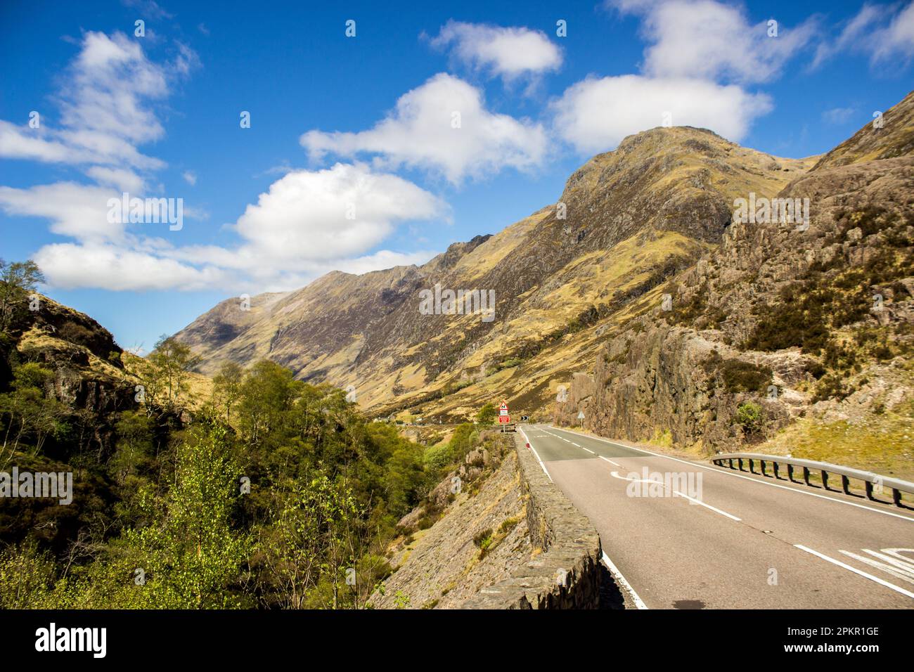 Strada che attraversa la Glen Coe Valley con le aspre montagne Grampian che si innalzano accanto ad essa Foto Stock