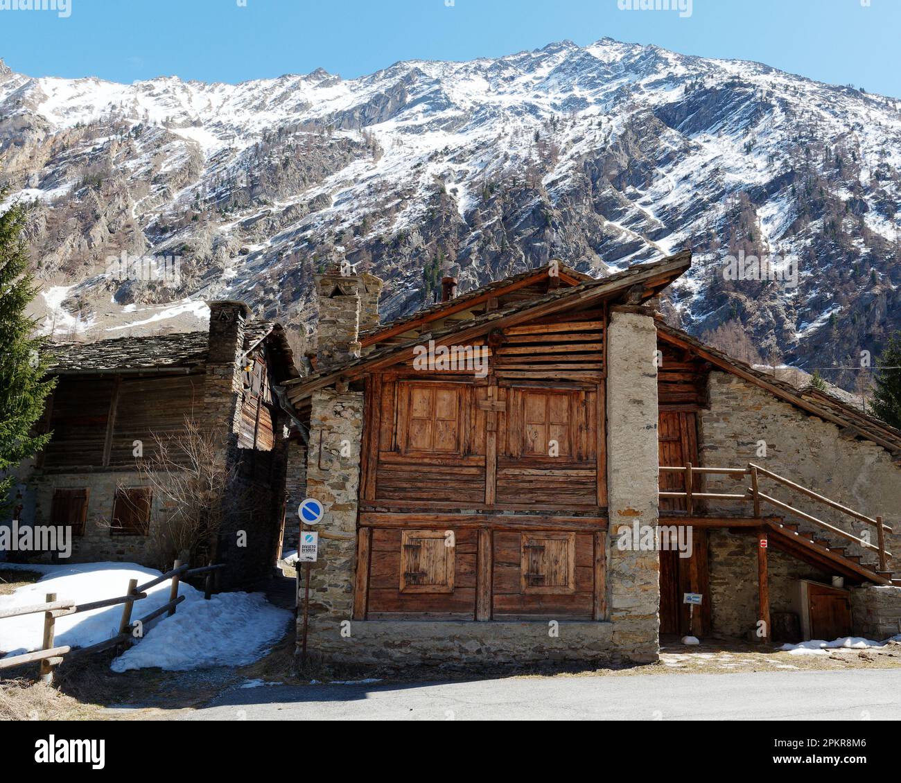 Tradizionale edificio in legno e pietra sotto una montagna innevata a Valnoney nel Parco Nazionale del Gran Paradiso, Valle d'Aosta, Italia Foto Stock