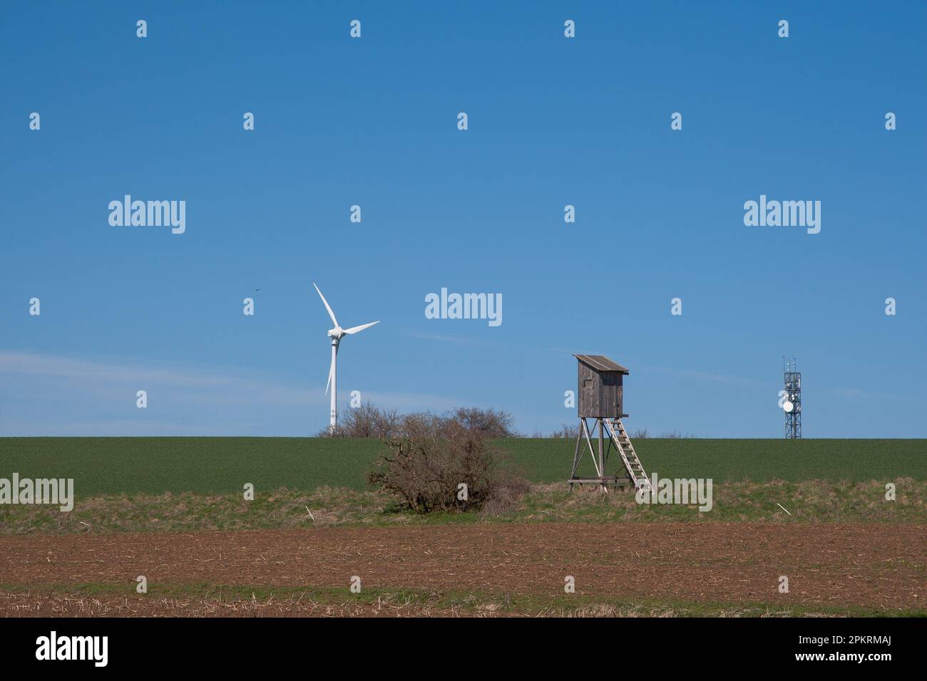 Un pulpito da caccia circondato da turbine eoliche e torri di trasmissione. Foto Stock