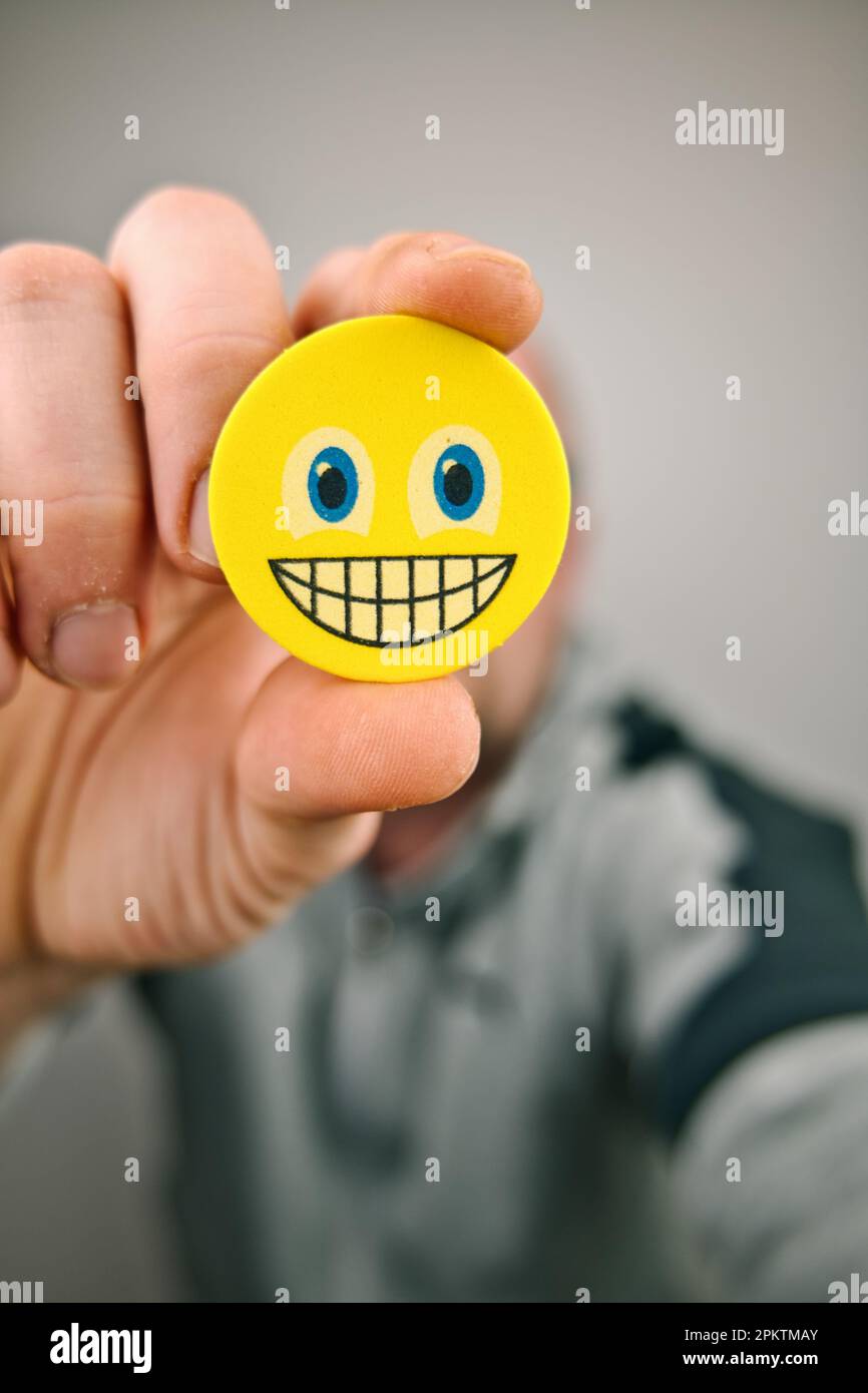 persona che tiene giallo sorridente faccia emoji davanti al suo volto Foto Stock