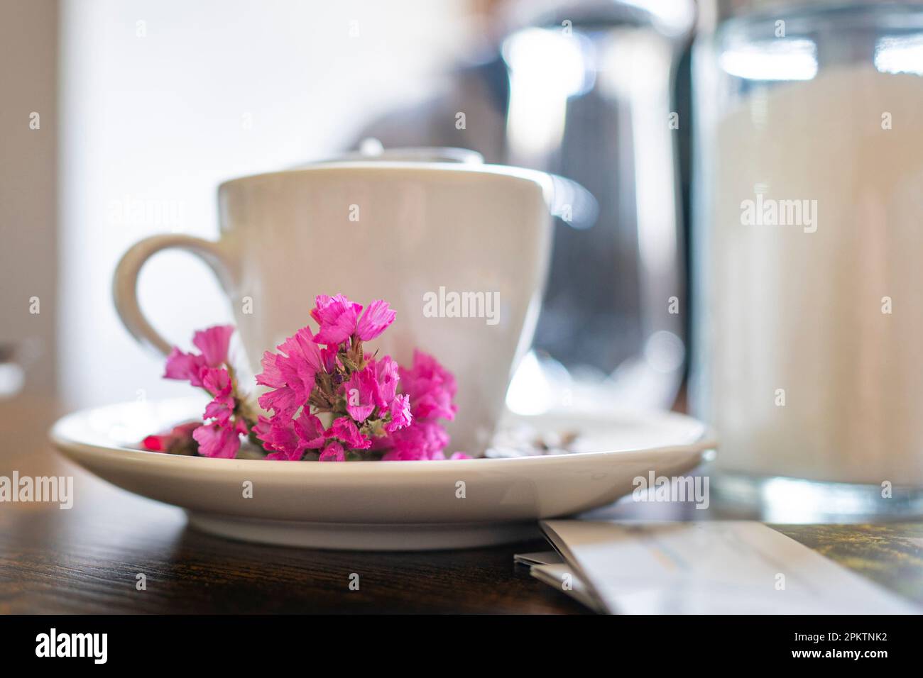 Tazza da caffè in porcellana bianca con fiori rosa su un tavolo di legno marrone. Ancora vita. Foto Stock