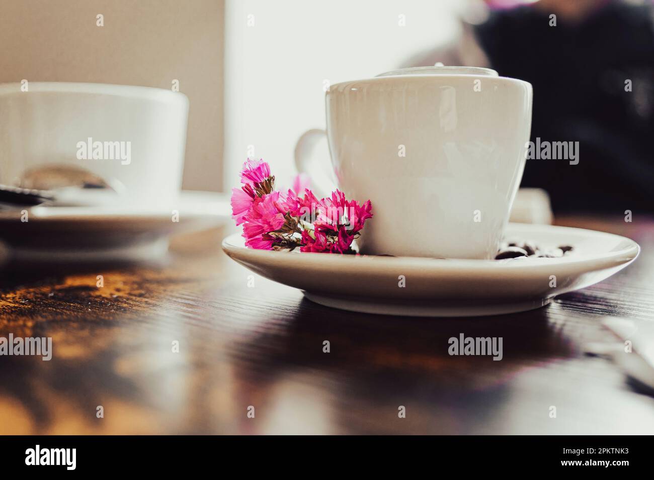 Tazza da caffè in porcellana bianca con fiori rosa su un tavolo di legno marrone. Ancora vita. Foto Stock