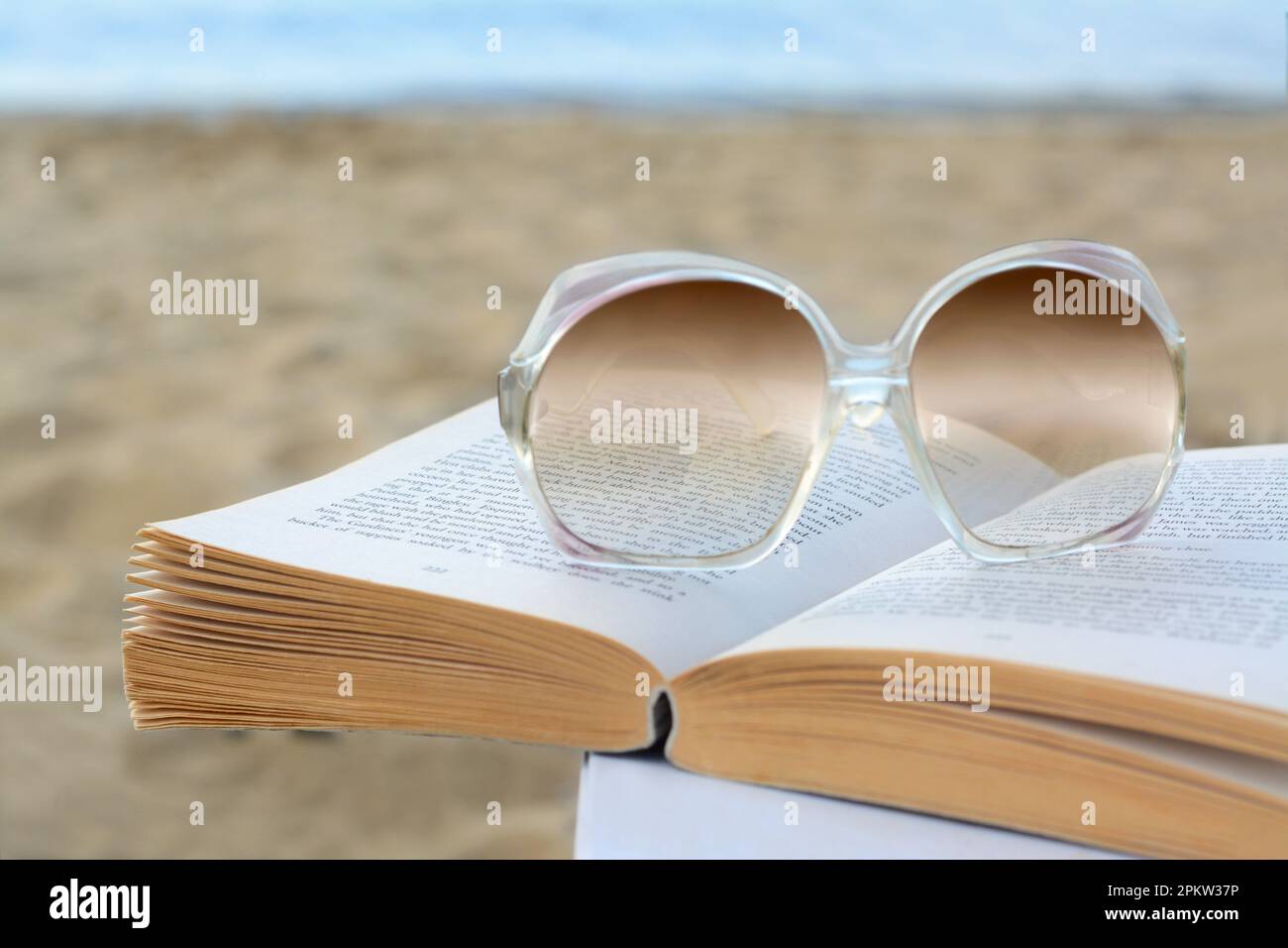 Libro aperto e occhiali da sole sulla spiaggia, primo piano Foto Stock