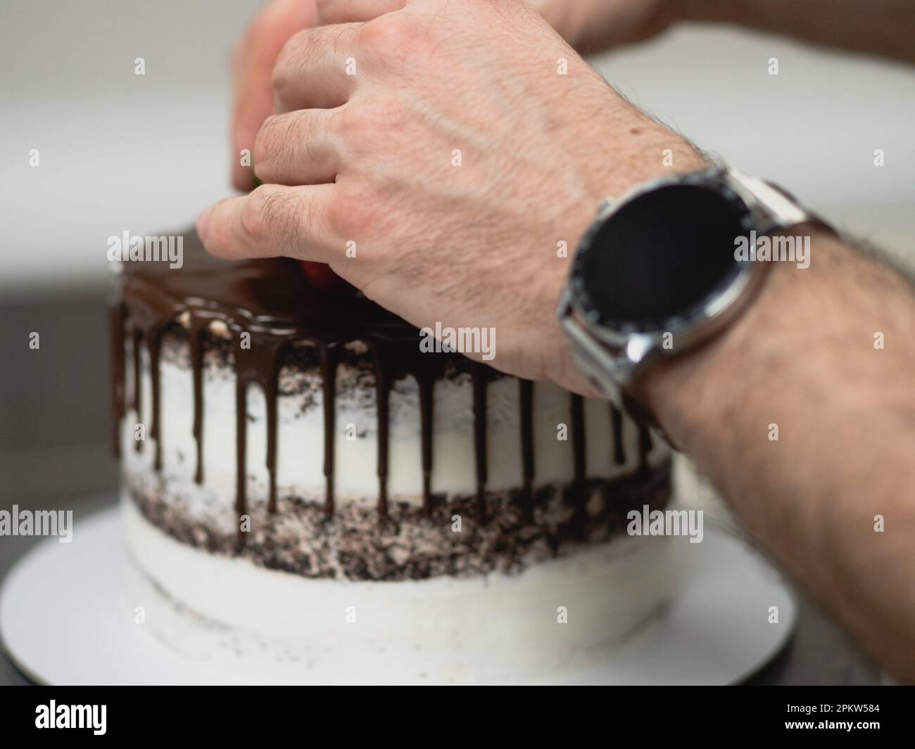 pasticcere preparare una torta glassata al cioccolato con gocce di frutta dolce e pennellate dorate Foto Stock