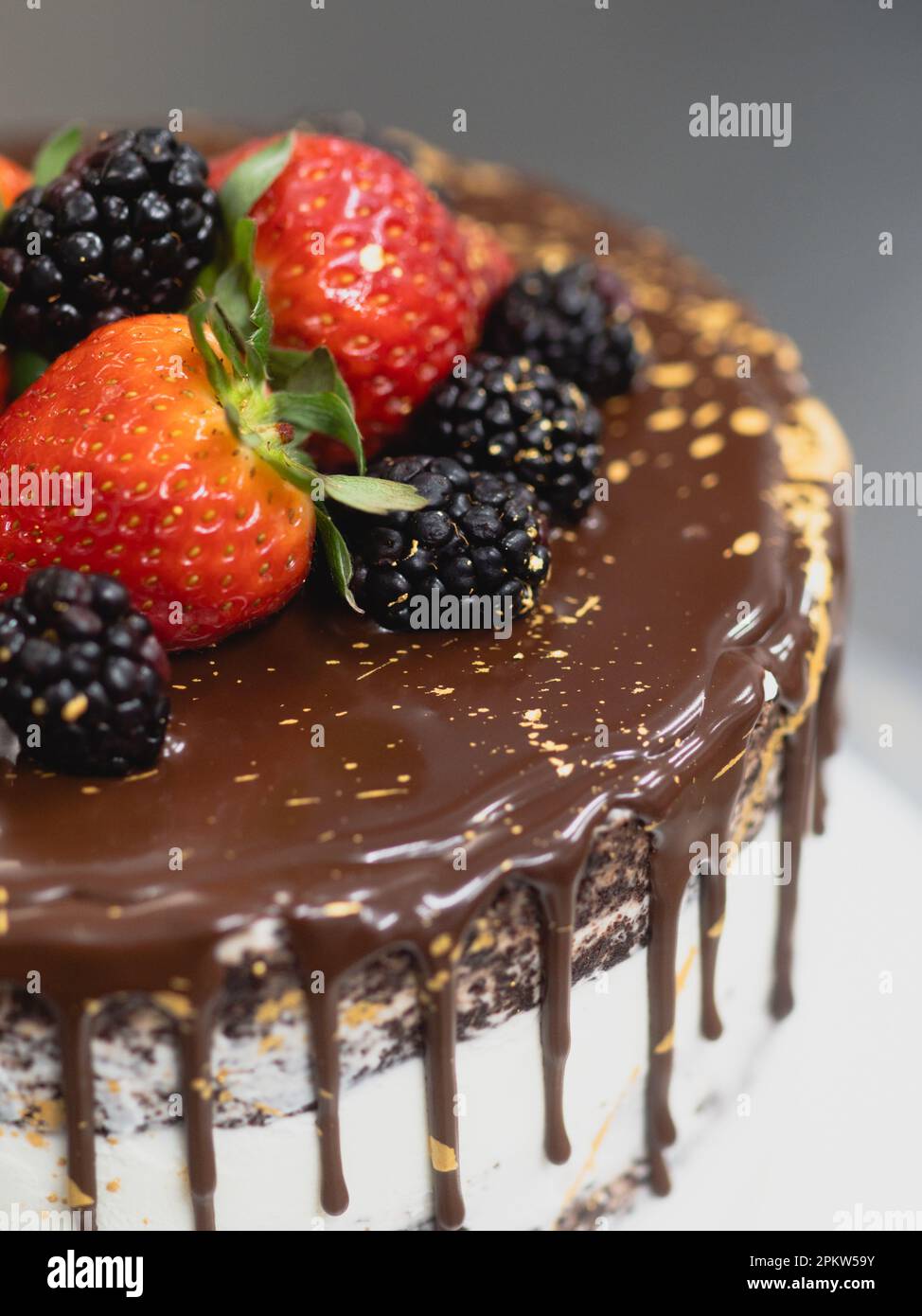 pasticcere preparare una torta glassata al cioccolato con gocce di frutta dolce e pennellate dorate Foto Stock