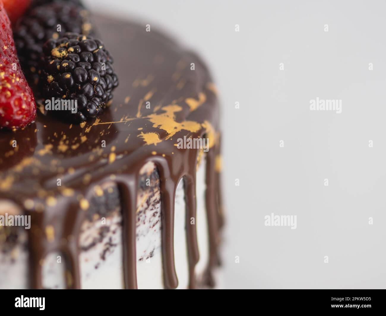 colpo da studio di torta glassata al cioccolato con gocce di frutta dolce e pennellate dorate Foto Stock