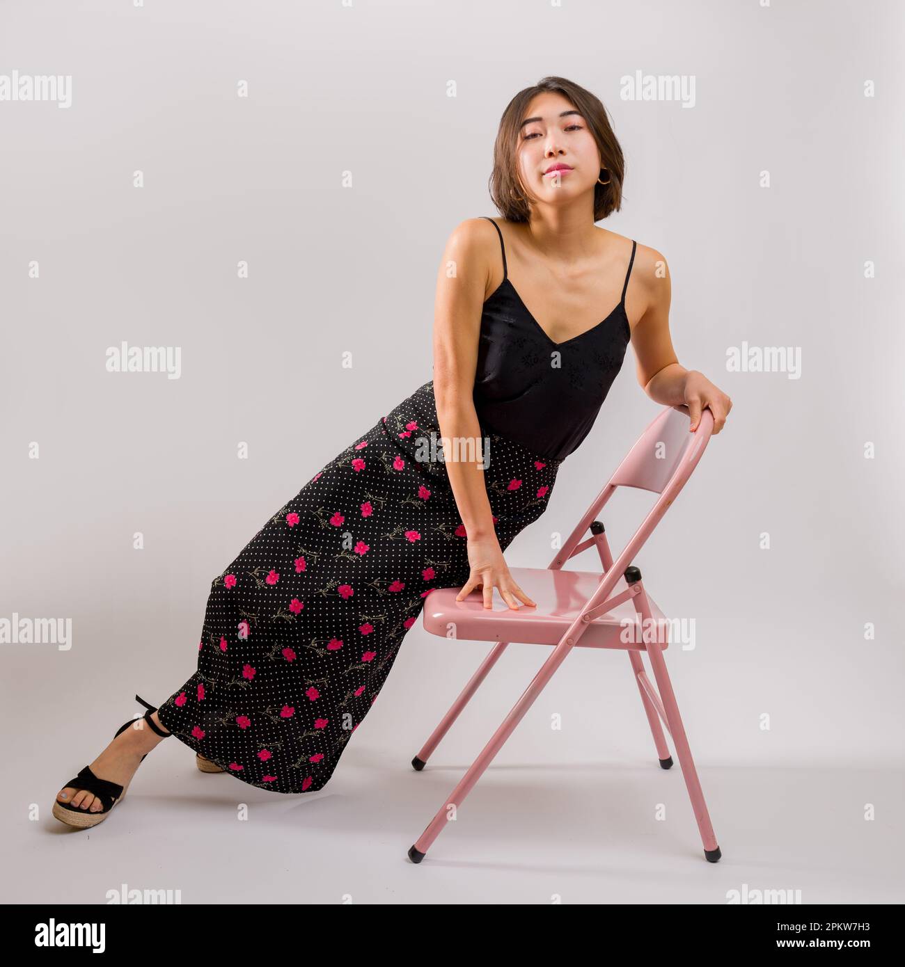 Giovane donna asiatica seduta su una sedia rosa in Studio | sfondo bianco | Abito con stampa floreale | Top in seta nera Foto Stock