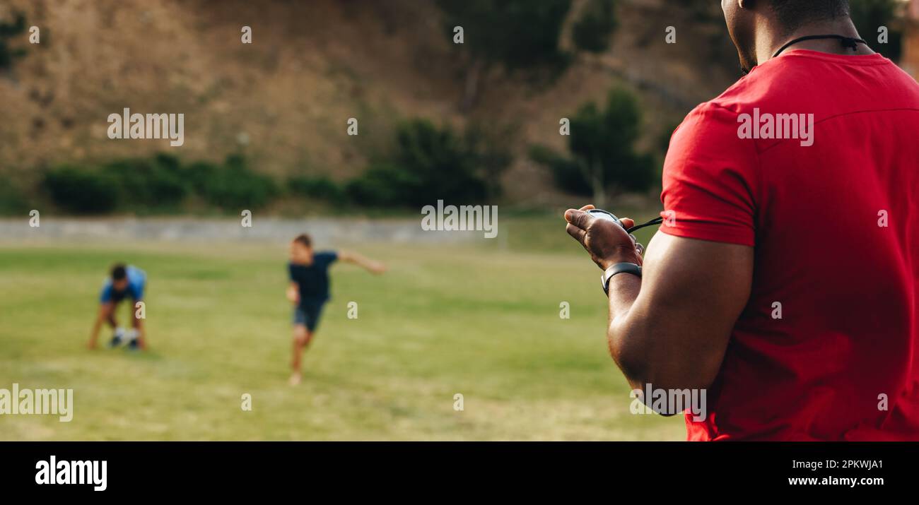 Uomo che istruisce i bambini della scuola in un terreno di sport. Allenatore di fitness con una sessione di riscaldamento con un gruppo di ragazzi della scuola elementare. Educazione sportiva in s Foto Stock