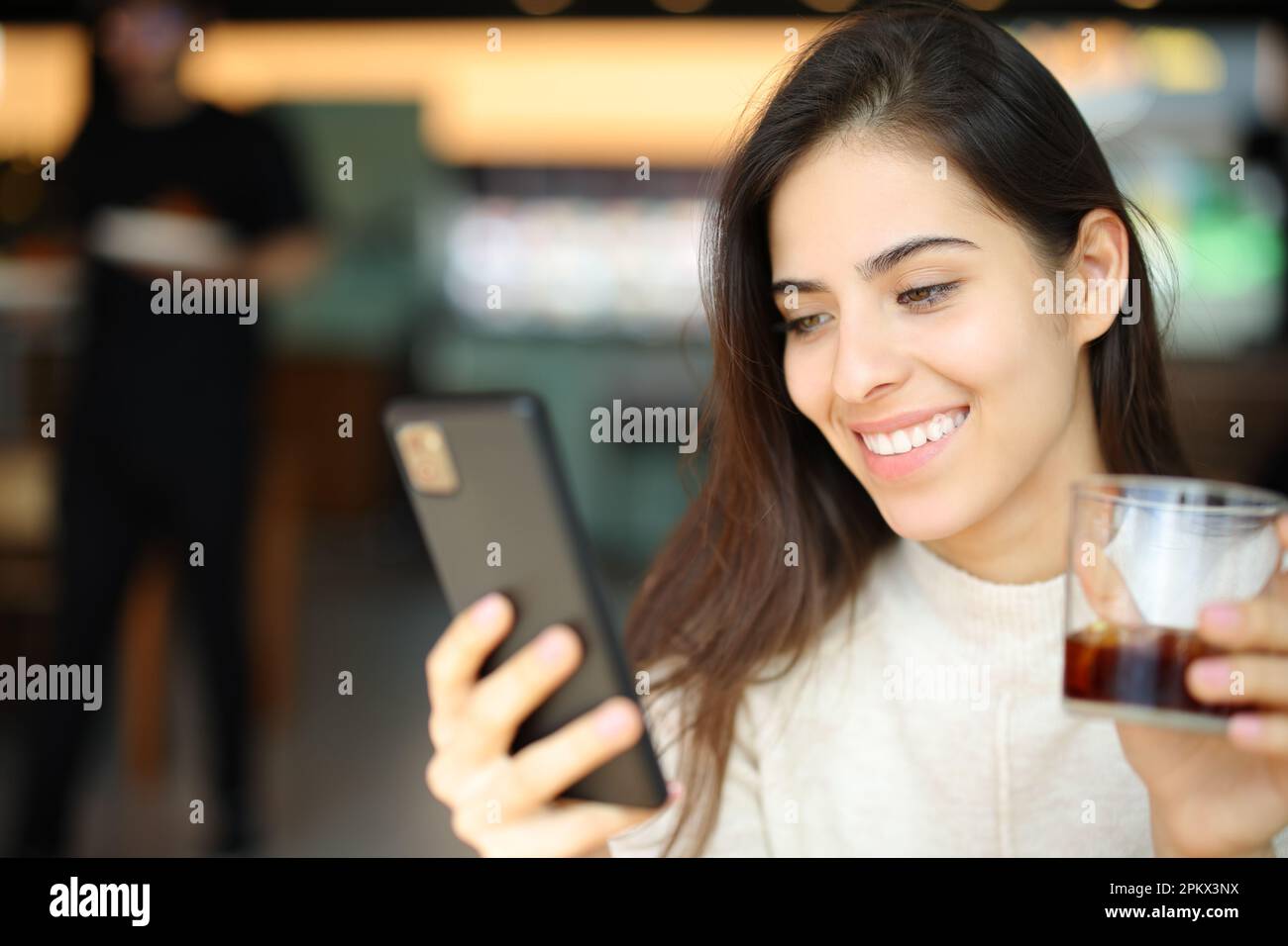 Cliente felice che controlla il telefono delle cellule che tiene la soda in un ristorante Foto Stock