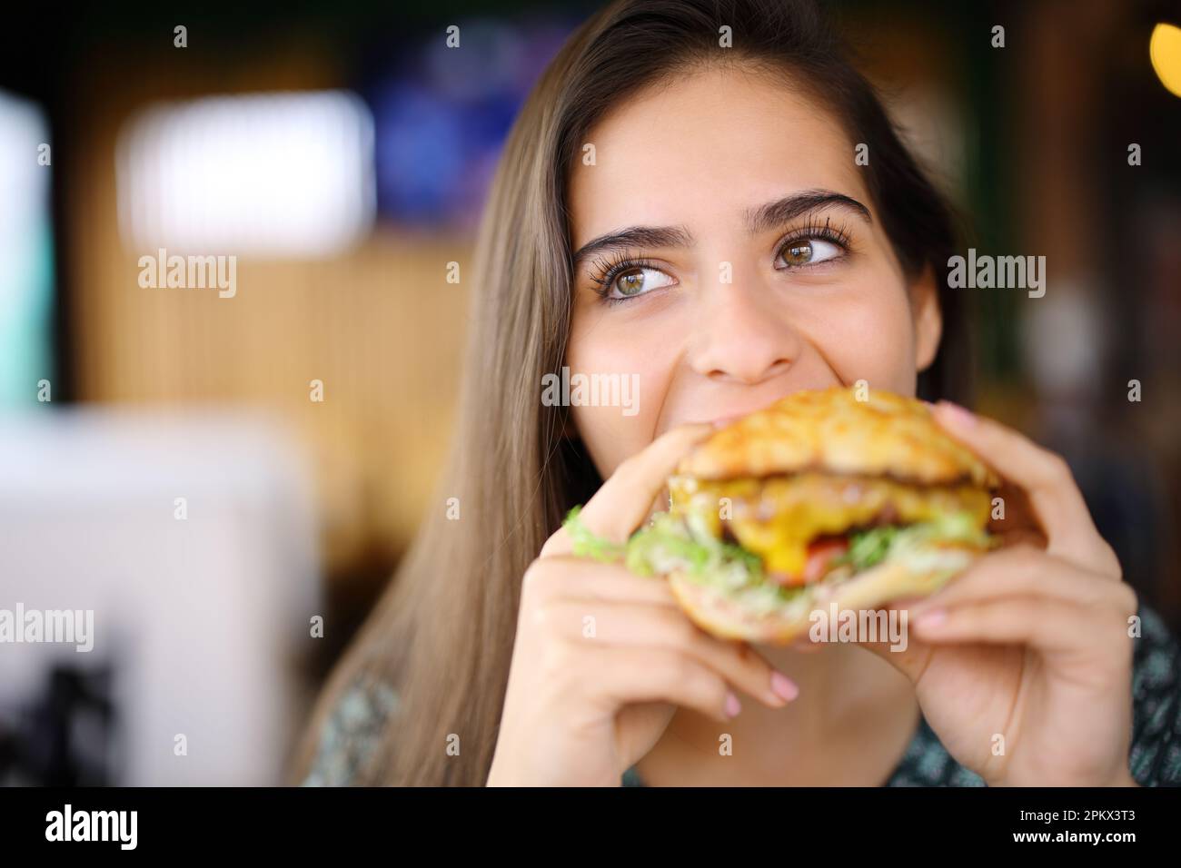 Vista frontale di una donna felice che mangia un grande hamburger in un ristorante Foto Stock