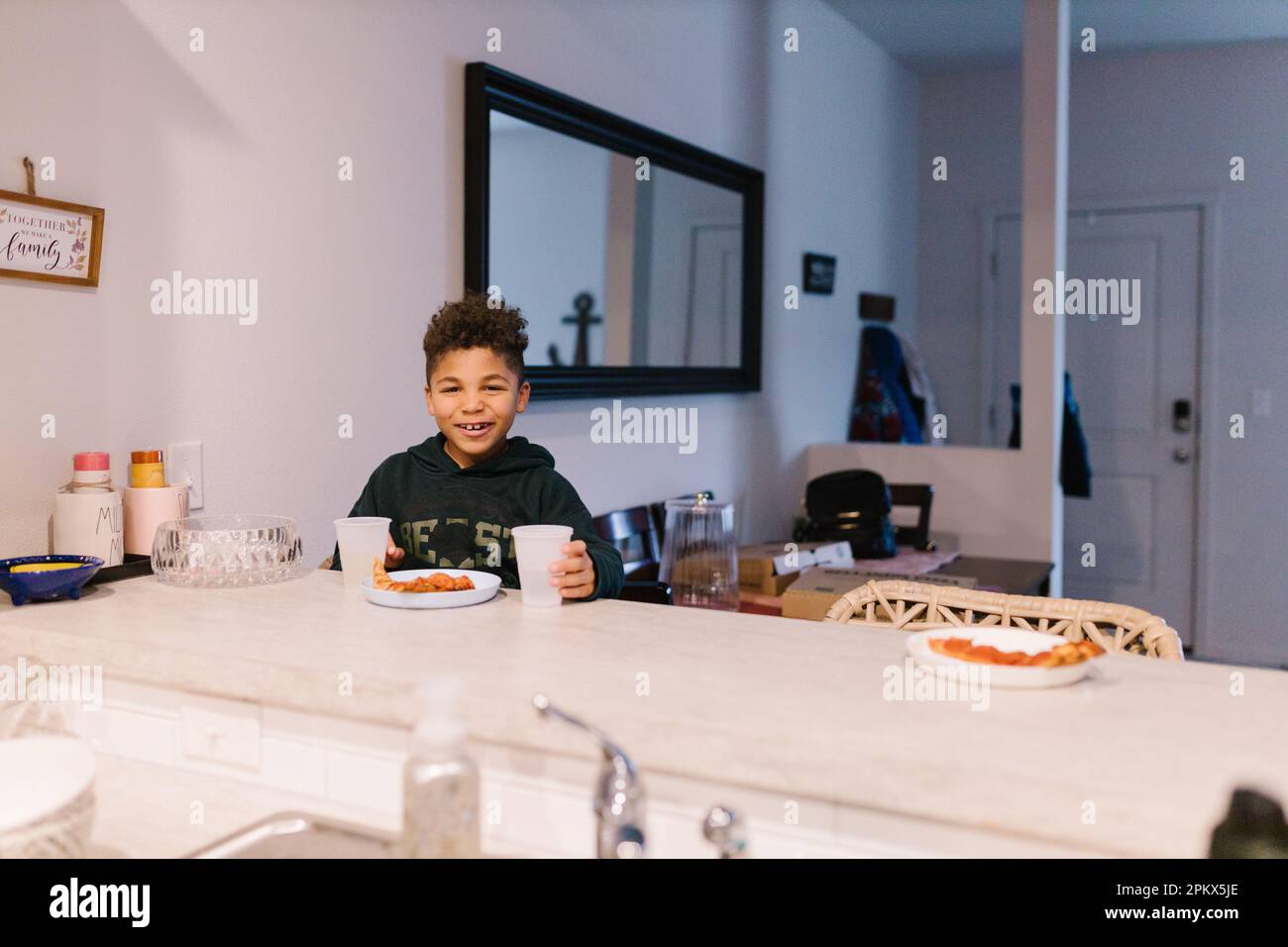 Felice bambino di corsa mista seduto al bancone che mangia la pizza Foto Stock