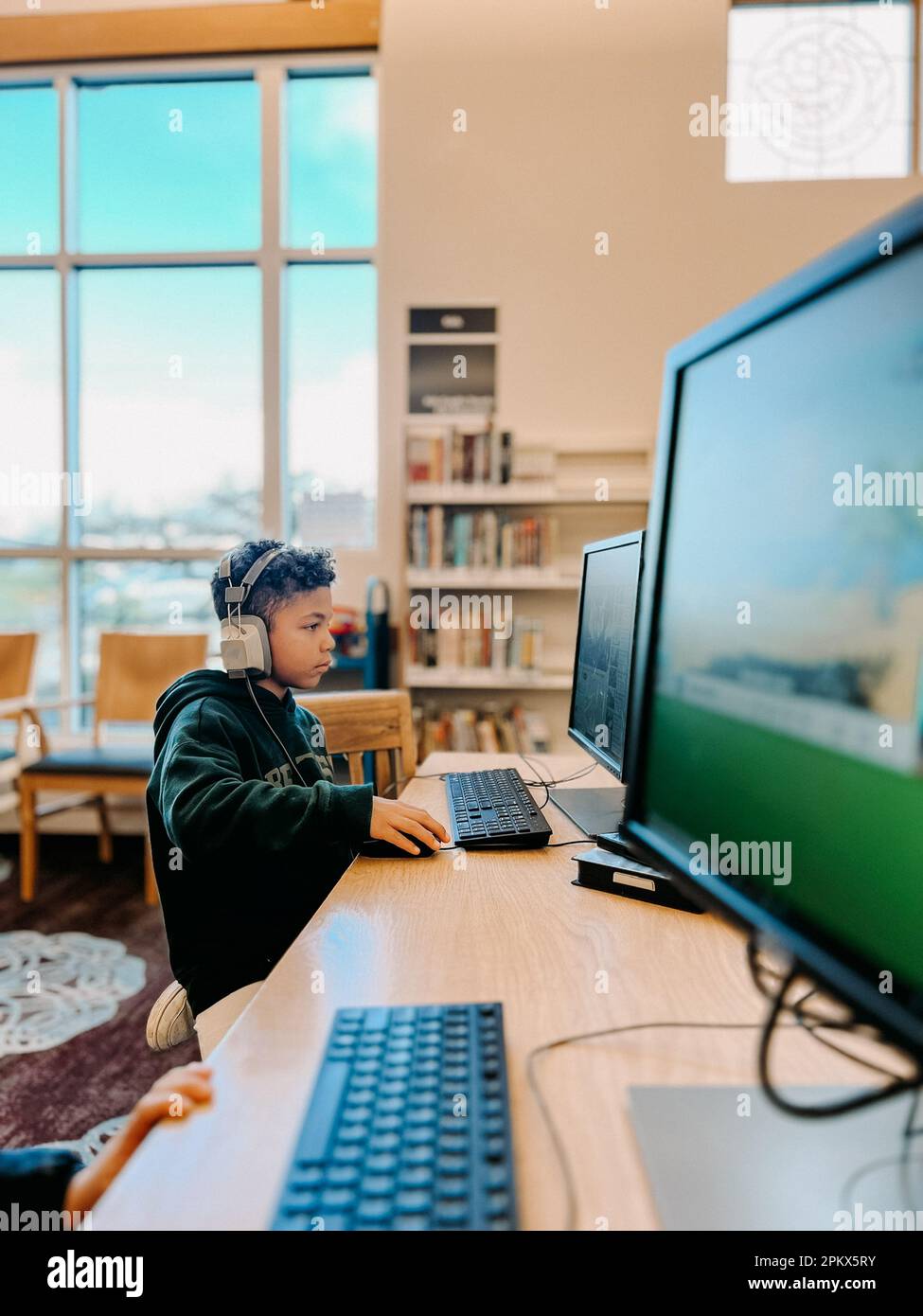 Capretto misto di corsa che si concentra sullo schermo del calcolatore alla biblioteca Foto Stock