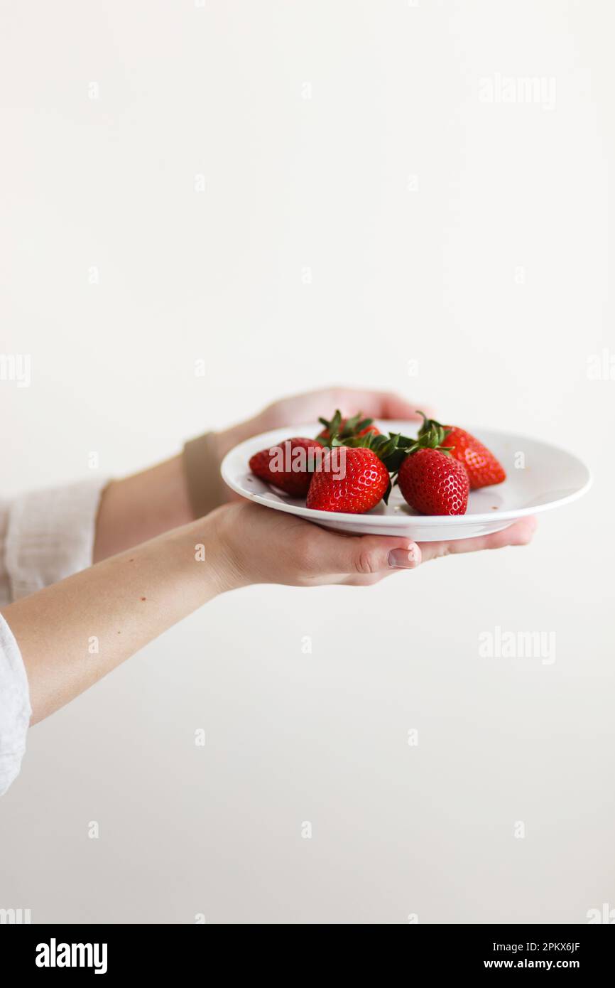 donna cuoco tiene in mano un piatto con fragole fresche rosse Foto Stock