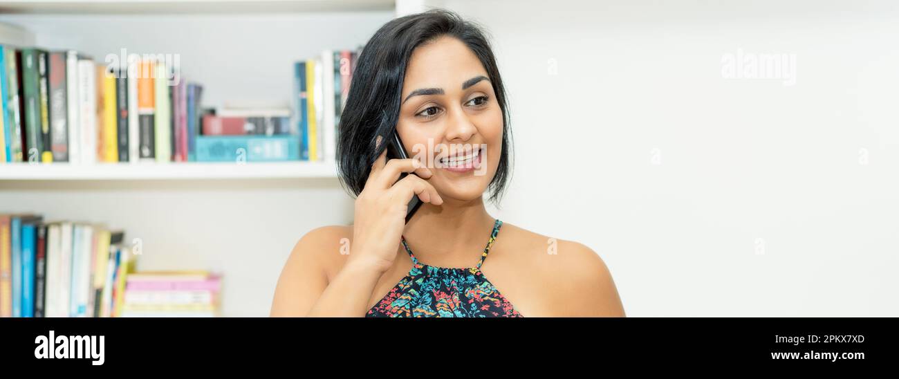 Bella messicana donna adulto maturo che parla al telefono al chiuso a casa Foto Stock