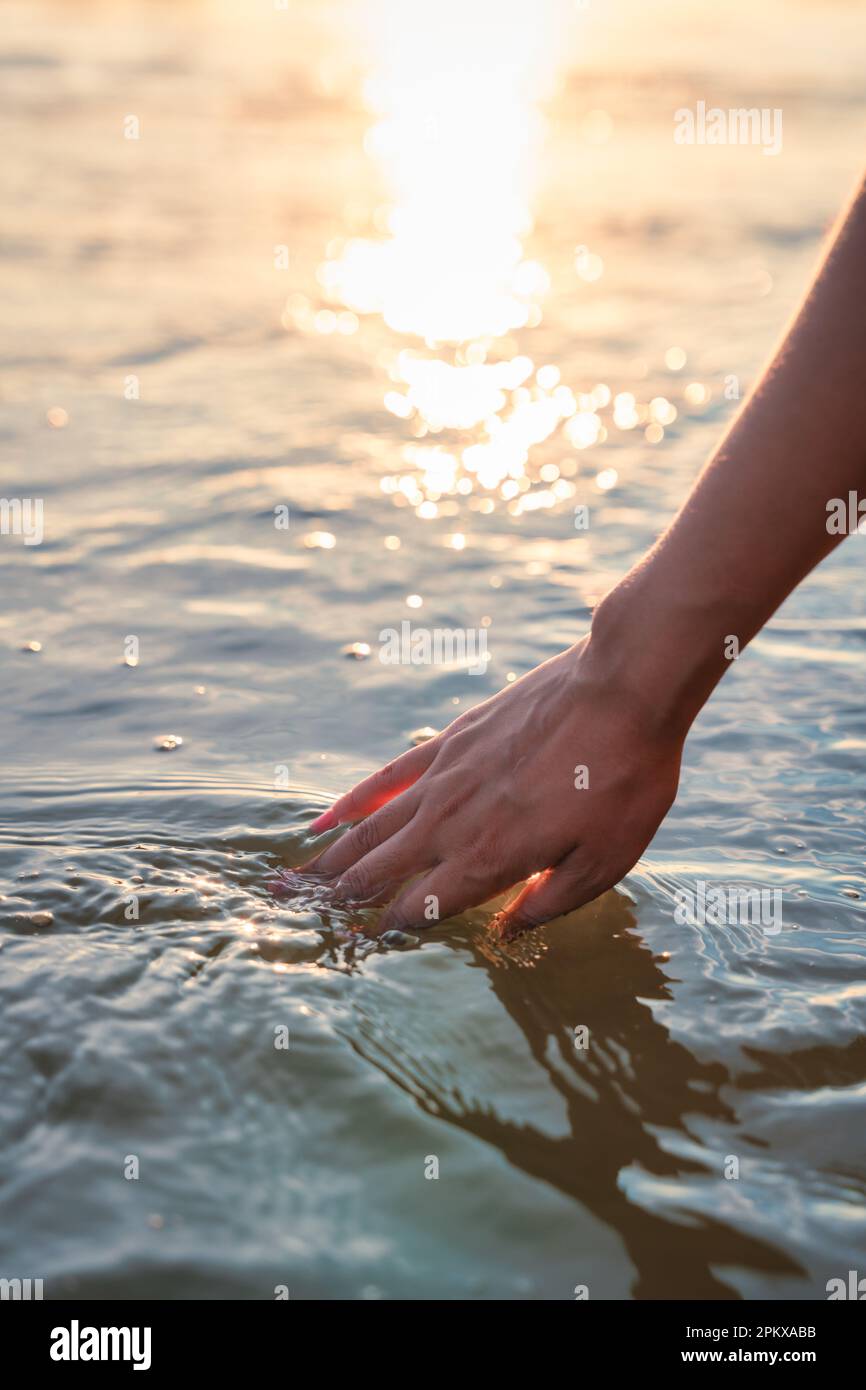 Mano di donna che tocca la superficie dell'acqua durante il tramonto Foto Stock