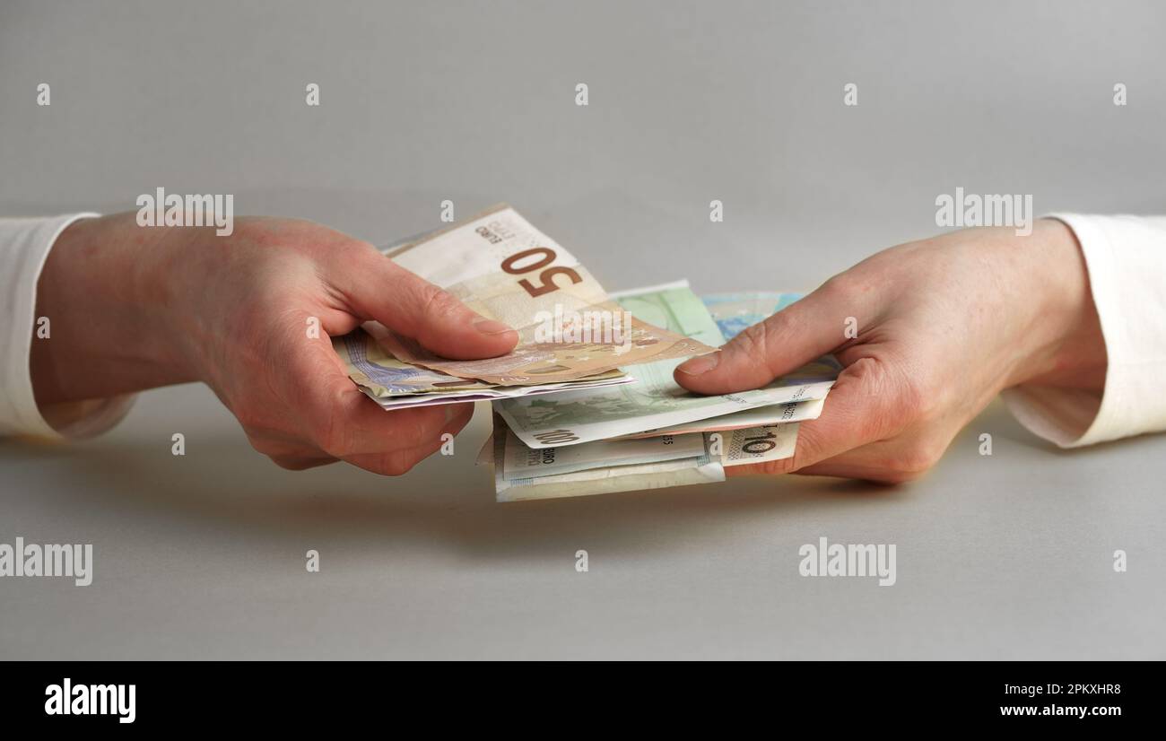 Mani e denaro. Le mani delle donne tengono, contano i soldi in euro e dollari isolati su uno sfondo grigio Foto Stock