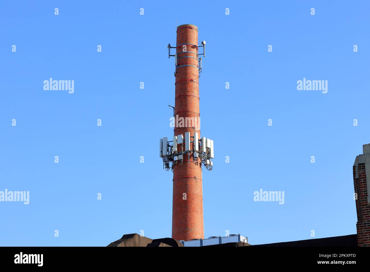 Apparecchiature per telecomunicazioni e antenne per cellulari installate su un camino industriale in muratura in mattoni trasformandolo in una torre per cellulari Foto Stock