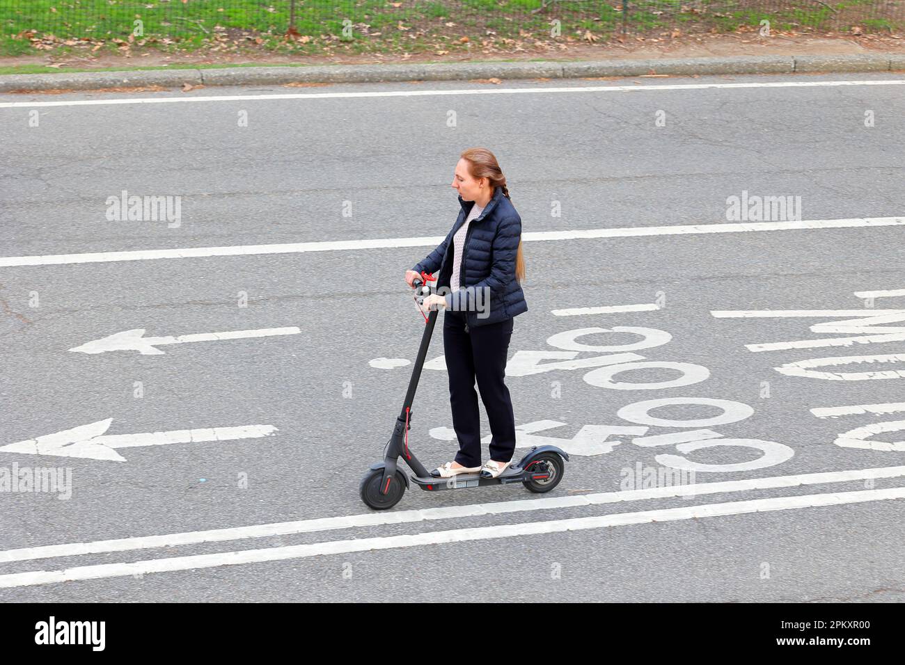 Una donna che si trova a New York per tornare a casa dal lavoro su uno scooter elettrico Foto Stock