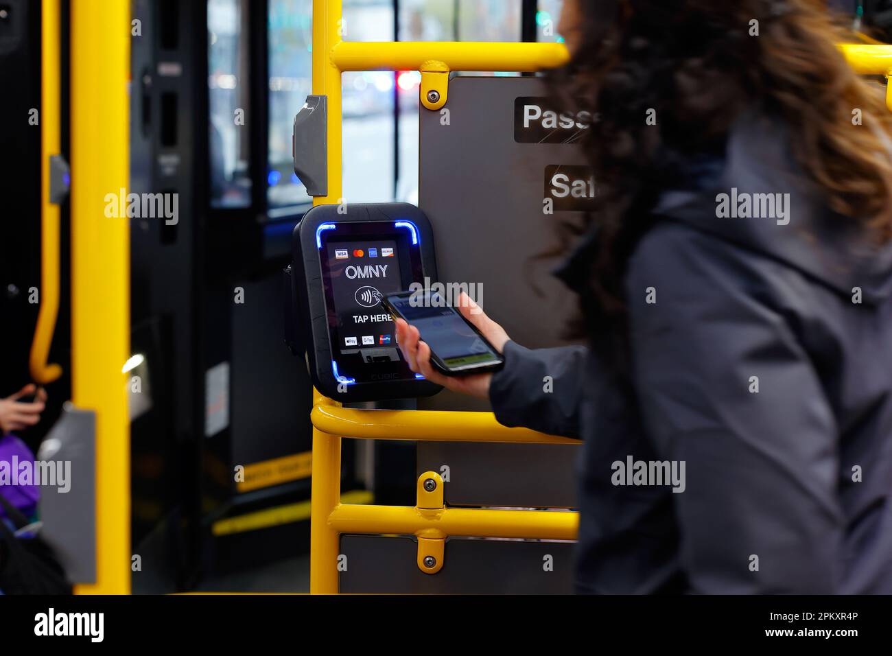 Una persona tocca uno smartphone a un lettore di pagamenti senza contatto OMNY su un autobus NYC Transit. Il lettore accetta pagamenti EMV tramite NFC Foto Stock