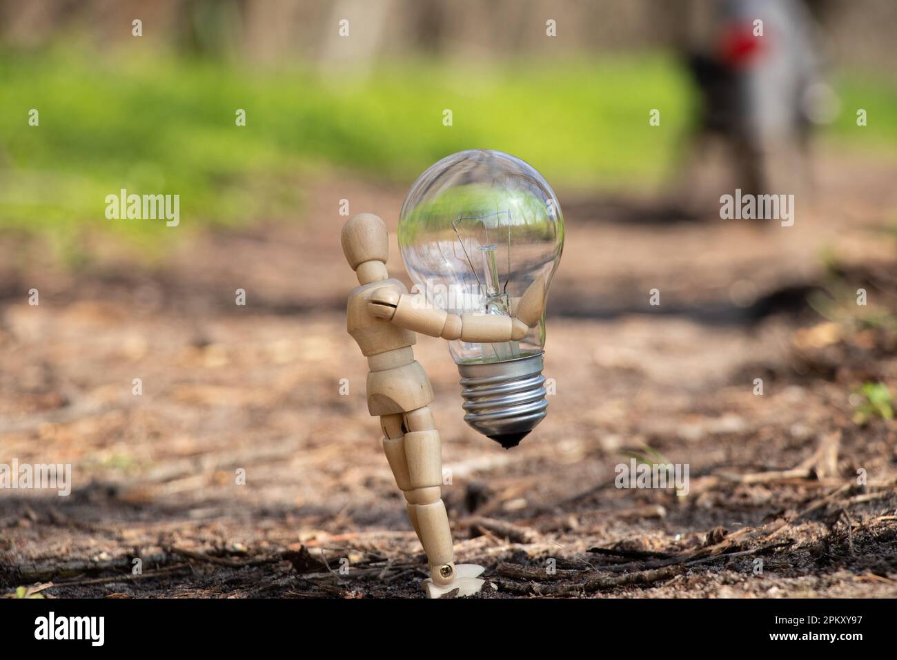 Un piccolo uomo di legno tiene una lampadina incandescente sull'erba nei parchi in Ucraina , elettricità Foto Stock