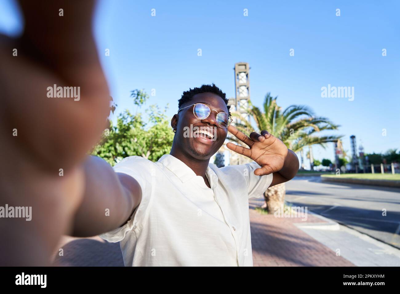 Felice giovane africano che prende un selfie guardando la macchina fotografica e agitando esso, condivisione di social media. Foto Stock