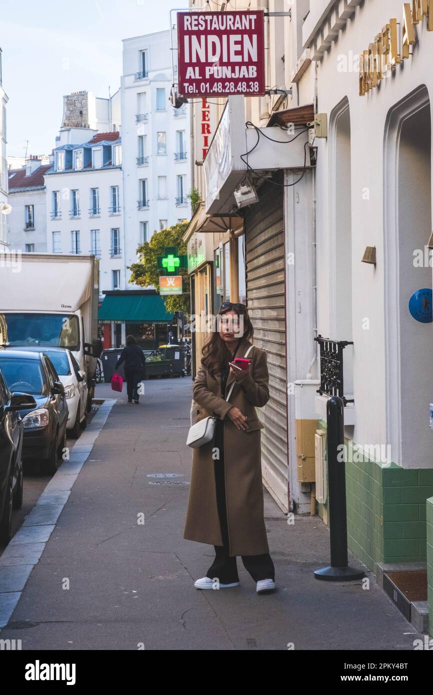 Giovane bella donna indossa un cappotto e una borsa laterale bianca - guarda alla macchina fotografica - Parigi, Francia Foto Stock