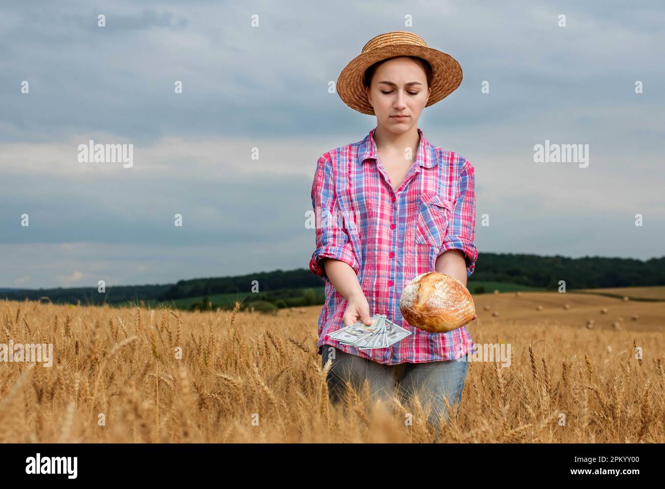 Giovane agricoltore che tiene dollari e pane in campo di grano dorato. Profitto dall'agricoltura durante la stagione di raccolta in estate. Foto Stock