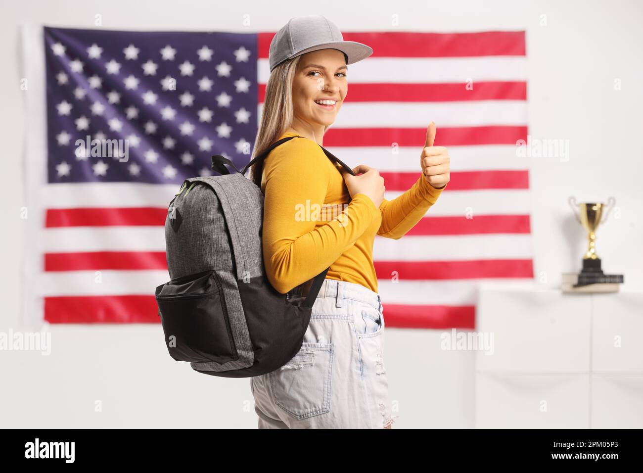 Studentessa con uno zaino che mostra i pollici davanti alla bandiera degli Stati Uniti Foto Stock