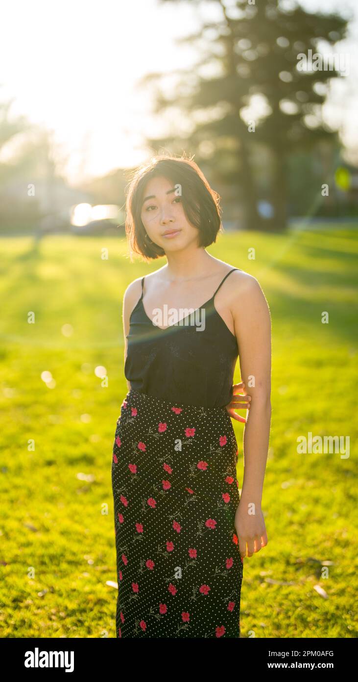 Giovane donna asiatica in piedi in un campo d'erba al Golden Hour | Moody Foto Stock