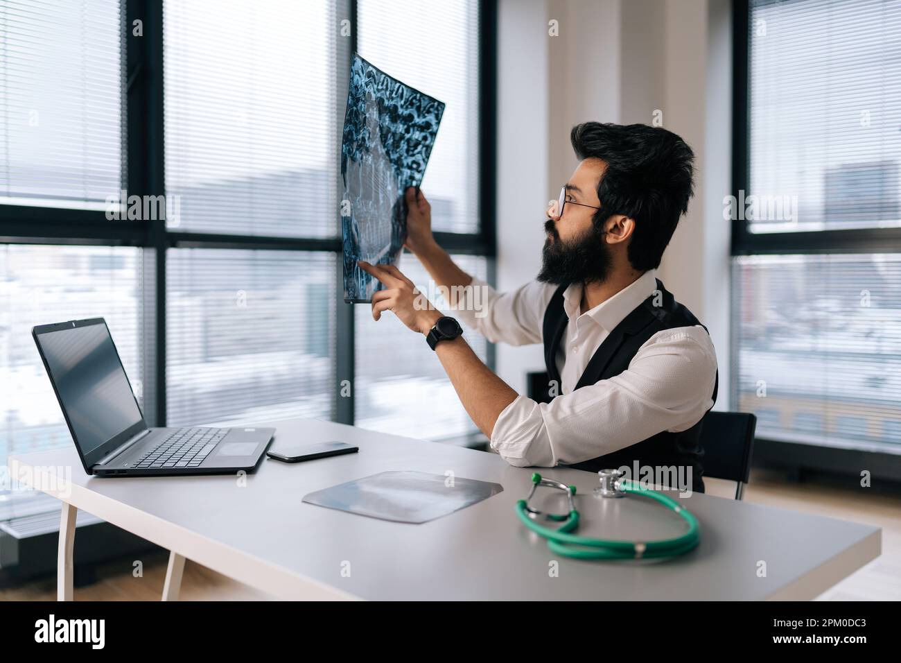Ritratto di un medico indiano maschio punteggiato bearded in occhiali pensando alla diagnosi guardando le immagini MRI scansione per finestra. Foto Stock