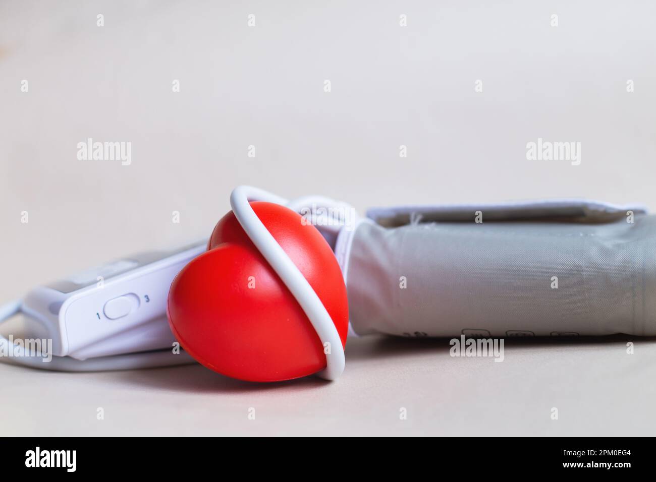 Tonometro elettronico bianco e cuore rosso isolato su sfondo beige. Misurazione della pressione, sanità e medicina, cardiologia e ipertensione pro Foto Stock