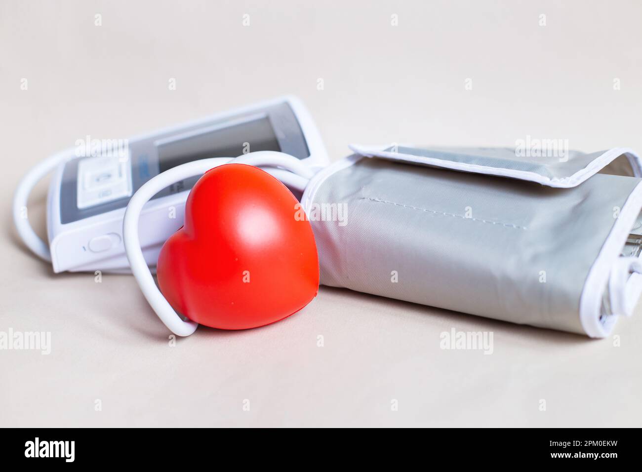 Tonometro elettronico bianco e cuore rosso isolato su sfondo beige. Misurazione della pressione, sanità e medicina, cardiologia e ipertensione pro Foto Stock