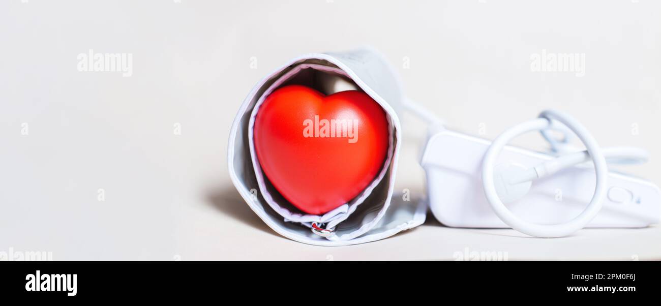 Tonometro elettronico bianco e cuore rosso isolato su sfondo beige. Misurazione della pressione, sanità e medicina, cardiologia e ipertensione pro Foto Stock