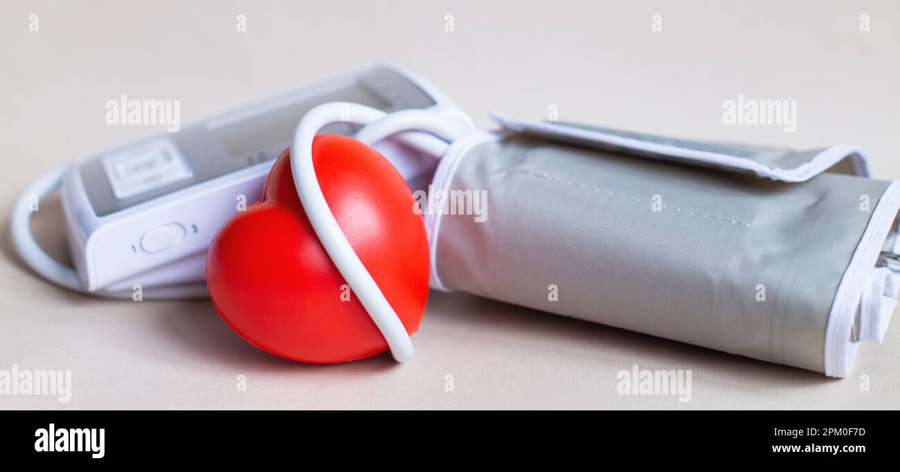 Tonometro elettronico bianco e cuore rosso isolato su sfondo beige. Misurazione della pressione, sanità e medicina, cardiologia e ipertensione pro Foto Stock