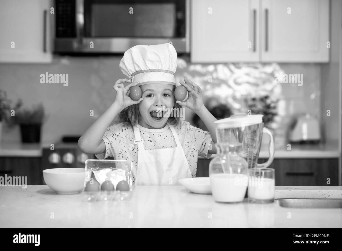 Cuoco di bambino cuoco con le uova. Cuoco del capretto cuoco nel cappello del cuoco che prepara il cibo sulla cucina. Bambino che rende gustoso delizioso. Cucina pasto. Foto Stock