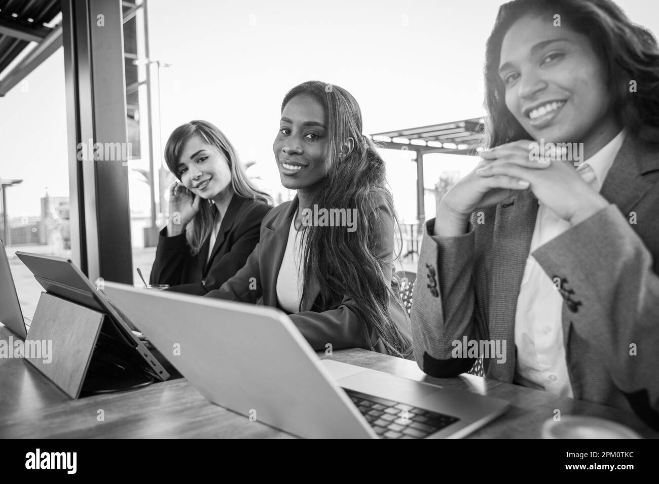 Tre donne d'affari sorridenti lavorano con i loro computer, foto in bianco e nero. Foto Stock