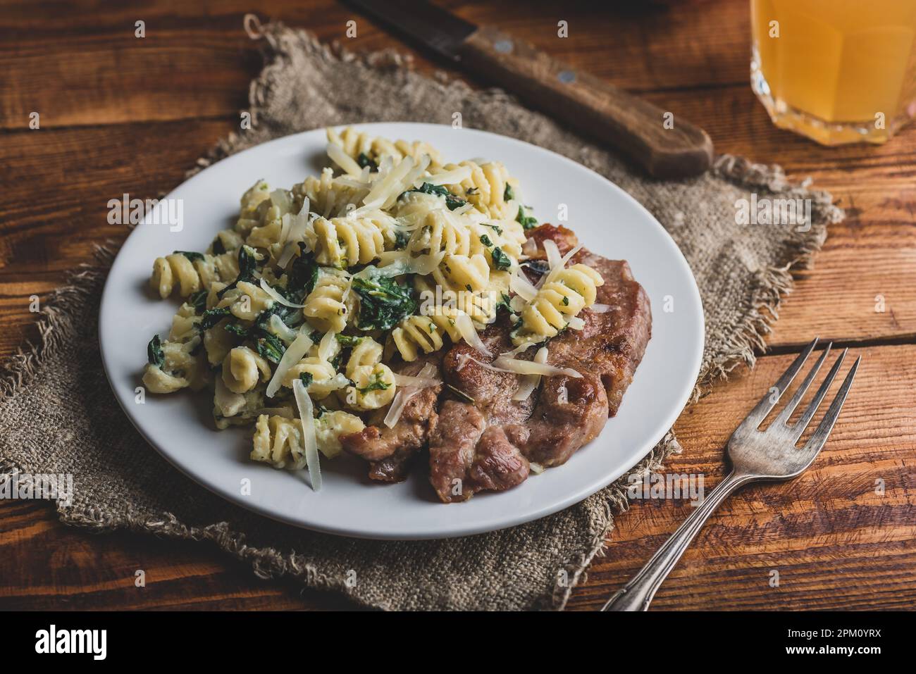 Bistecca di maiale e pasta cremosa di spinaci guarnita con parmigiano Sulla piastra bianca Foto Stock