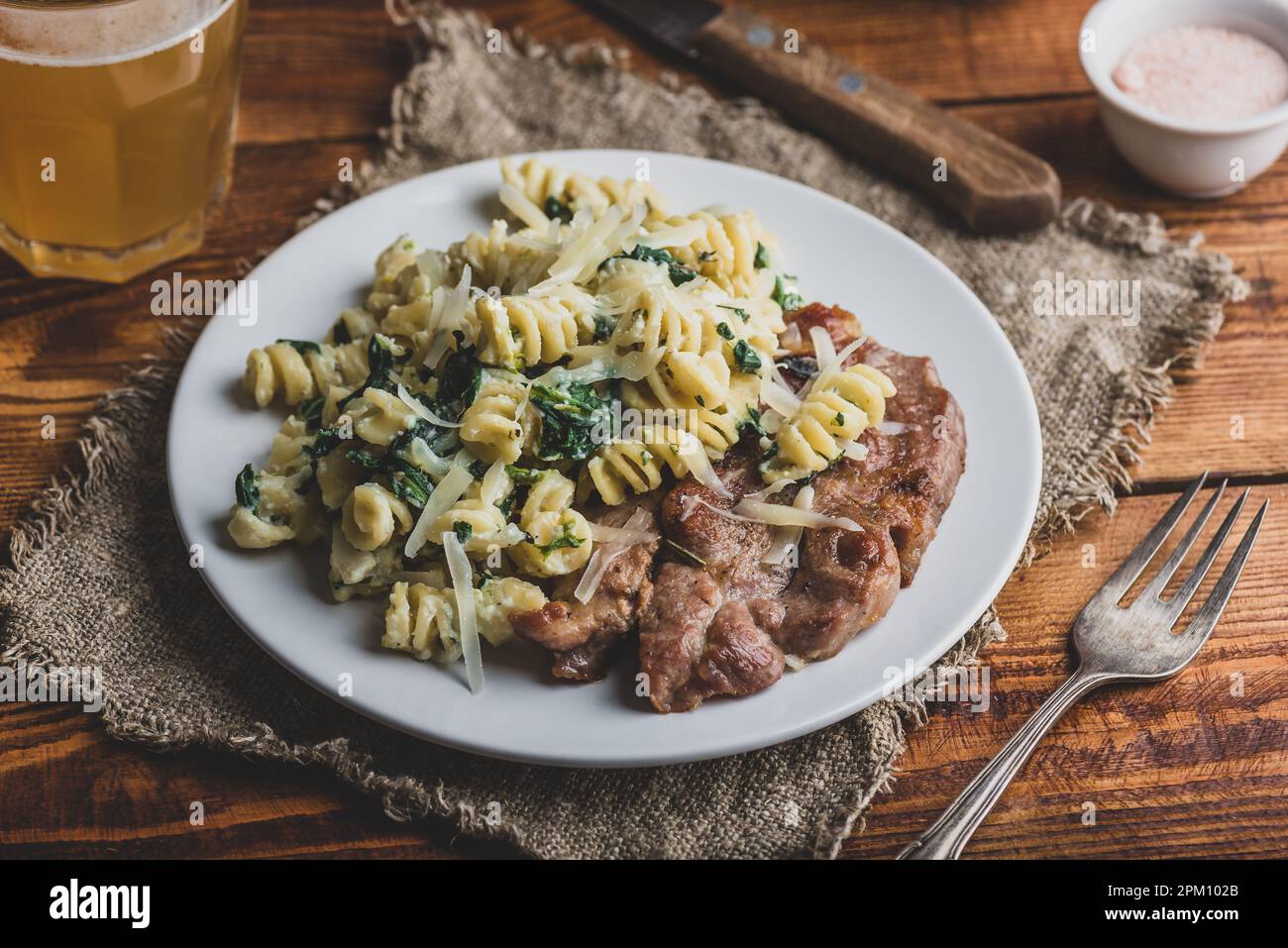 Bistecca di maiale fritta e pasta di spinaci con ricotta e parmigiano Formaggio su piatto bianco Foto Stock