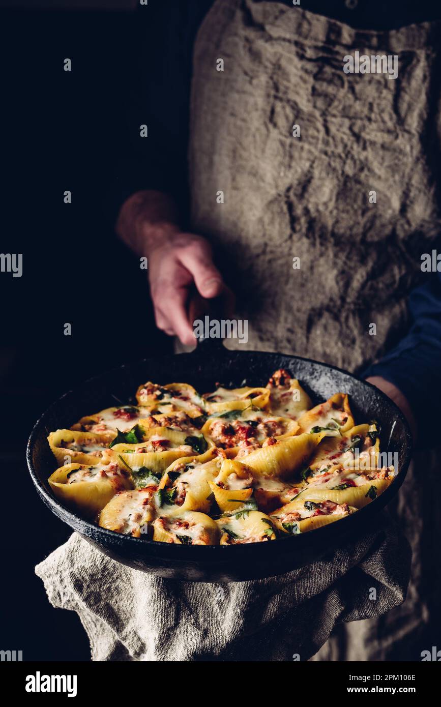 Lo chef conserva la padella di conchiglie di jumbo al forno ripieni di manzo macinato, spinaci e formaggio Foto Stock