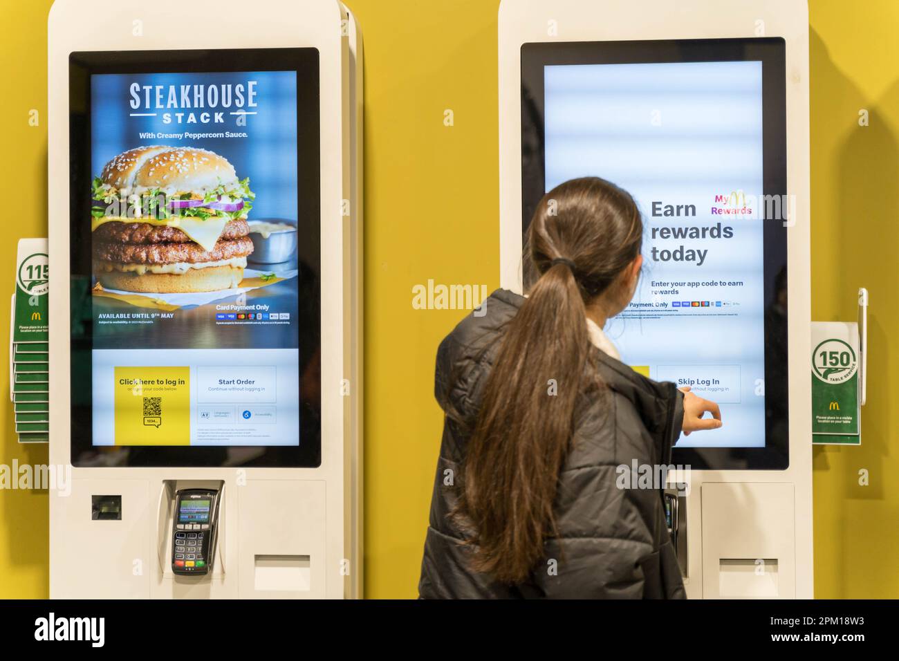 Donna cliente che ordina cibo su un sistema di ordinazione con schermo a sfioramento LED al ristorante McDonald's, un altro schermo che mostra STEAKHOUSE Stack Inghilterra UK Foto Stock