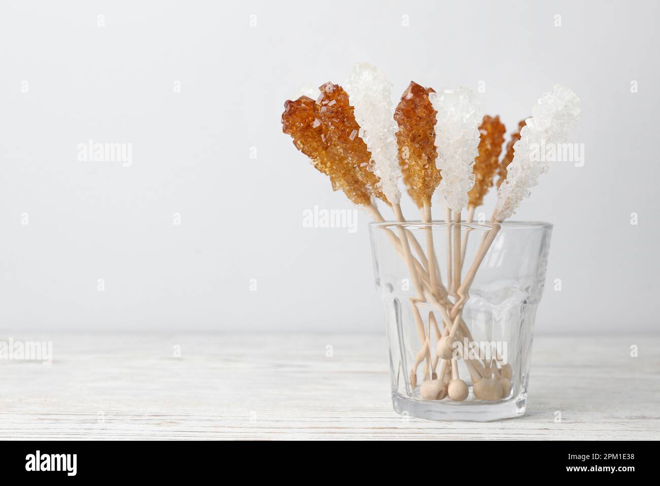 Bastoncini con cristalli di zucchero in vetro su tavolo di legno bianco, spazio per il testo. Gustose caramelle di roccia Foto Stock