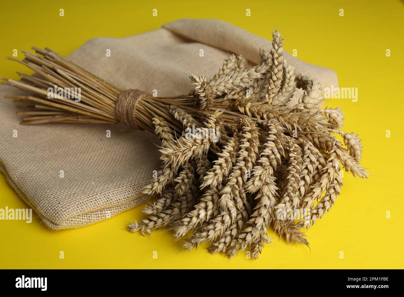 Mazzo di grano e sacco su fondo giallo Foto Stock